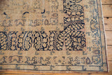 Worn texture of vintage Kerman carpet corner, showing navy millefleur border and antique ivory field with visible foundation.