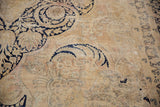 Distressed vintage Kerman carpet showing faded ivory field, deep navy vinery, and floral motifs.