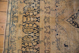Visible threadbare areas and dark navy scrolling vinery on the distressed vintage Kerman rug.