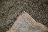 Folded corner of an antique distressed Persian Malayer rug showing faded navy patterns, beige foundation, and fringe.