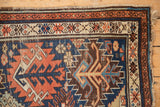 Antique Kuba rug corner with indigo, madder red, ivory geometric patterns, visible wear, and intact selvage.