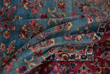 Folded vintage Kerman carpet showing sky blue field, wine red border, and millefleur motifs.
