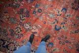 Feet on distressed Mahal carpet with brick red floral field and visible foundation wear.