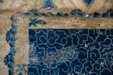 Distressed antique Peking rug corner: cobalt blue cloudband border and worn beige field, exposed foundation.