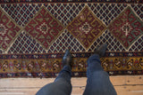 Close view of the vintage Caucasian runner's worn texture and geometric diamond pattern in red, blue, and gold.