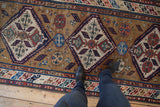 Detailing the antique Caucasian runner's low-pile texture across its geometric diamond medallions.