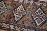 Angled view of the antique Caucasian runner's ochre field, diamond medallion, and geometric serpent border.