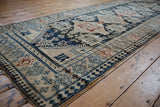 Low angle on a distressed Karabagh runner highlighting the short, even pile and geometric pawn motif border.