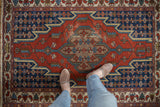 Vintage Persian Hamadan rug with geometric medallion shown from a standing perspective for scale.