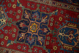 Vintage Heriz rug close-up: cherry red field, navy floral pattern, hook-latch motif, visible wear.