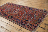 Brick red field with geometric blossoms and navy border on the vintage Heriz runner.