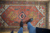 Vintage Heriz rug detail: rust field with geometric buds, serrated leaves, and minor seed pattern border.
