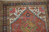 Vintage Heriz rug corner featuring madder rust field, geometric motifs, and a patterned seed design border.