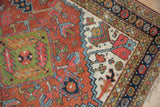 Hand-knotted Heriz rug close-up: navy floral cross-section with madder root rust and jade green.