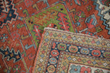 Folded vintage Heriz rug corner, showing geometric seed border and woven foundation.