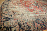 Close view of antique Serapi rug: worn brick red field, navy border, and visible foundation.