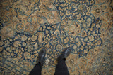 Distressed vintage Meshed rug showing navy and sand floral patterns, visible wear, and boots.