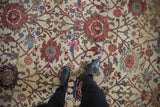 Feet on antique Mahal rug fragment, showing worn terra cotta vinery on ivory ground.
