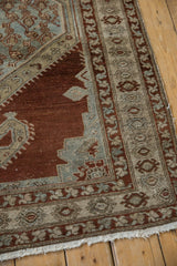 Distressed vintage Malayer rug corner with worn chestnut field and geometric border motifs.