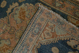 Folded corner of distressed Malayer rug showing dusty navy border and white fringe.