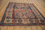 Corner of antique Caucasian rug with tattered fringe and worn sapphire blue, cherry red patterns.