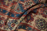 Folded antique Caucasian rug detail showing textured floral pinwheel and geometric.