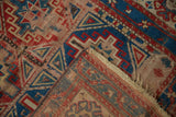 Folded antique Caucasian rug with geometric motifs, sapphire blue, red, and visible wear.