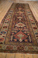 Serrated diamond medallions, abstract birds, and finned leaves on antique Kuba runner's navy field.