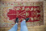 Distressed Oushak rug corner with cherry red field and pale sea foam floral vine border.