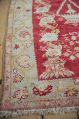 Distressed Oushak rug detail: Pale seafoam border with gold vines, cherry red field, and fringe.