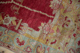 Distressed vintage Oushak rug featuring cherry red, gold, sea foam, and faded floral vine motifs.