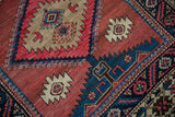 Checkered and serrated diamond motif with complex artistry in beige and blue on brick red.