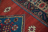 Cochineal red field, serrated blue medallion edge, and geometric pattern border.