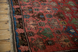 Close-up of antique Caucasian rug: dusty raspberry floral design, blue, green accents, and fringe.