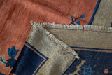 Folded corner of a Peking carpet reveals copper pile, blue floral, striped sand-colored back.