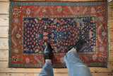 Detail of vintage Persian Hamadan rug showing tattered fringe, navy millefleur field, and red floral border.