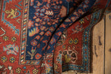 Folded vintage Hamadan rug, highlighting navy millefleur field and madder red floral border.