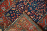 Folded vintage Hamadan rug corner showing madder root red border and navy floral patterns.