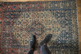 Antique Senneh rug's stepped medallion, navy Herati field, finned border, and visible abrashes.