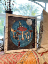 Dreamscape mixed media art with distressed white frame, full moon, and a figure on a red mushroom.