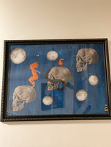 Welcome to the Universe mixed media art: skulls, moons, orange figure, dark blue field, ornate frame.