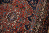 Vintage Qashqai carpet detail, madder root red field, navy border, geometric hook-and-latch motifs, visible wear.