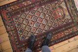 Antique Daghestan rug's primitive geometric patterns in ruby red, navy, and ivory underfoot.