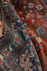 Close view of a vintage Abadeh rug's rolled navy border beside its intricate red floral field.