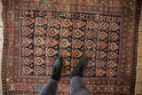Antique Caucasian rug's worn geometric field, detailed in navy, madder root, and celadon hues.