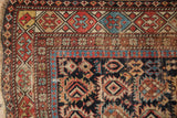 Antique Caucasian rug corner with geometric crab border, pawn motif, visible wear, madder root, navy, celadon.