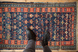 Antique Caucasian rug's cobalt blue field, brick red floral border, and geometric motifs, with boots.