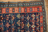 Antique Caucasian rug corner: cobalt blue field, brick red floral border, and worn fringe.