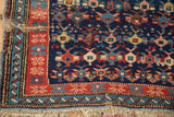 Antique Caucasian rug corner with brick red floral border, blue ribboned minor, and fringe.