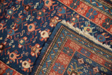Fringe, geometric brick red border, and cobalt blue field with visible knot heads.